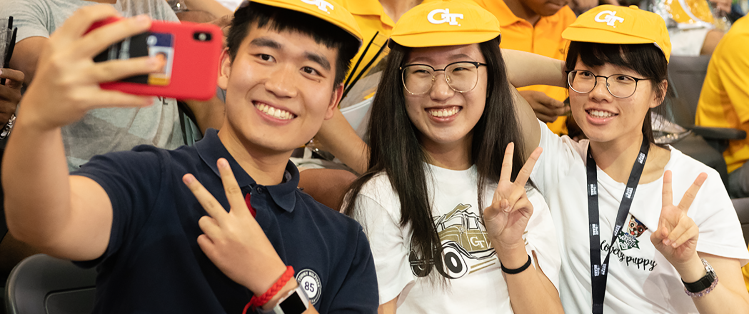 One young man and two young women wearing rat caps taking a selfie.